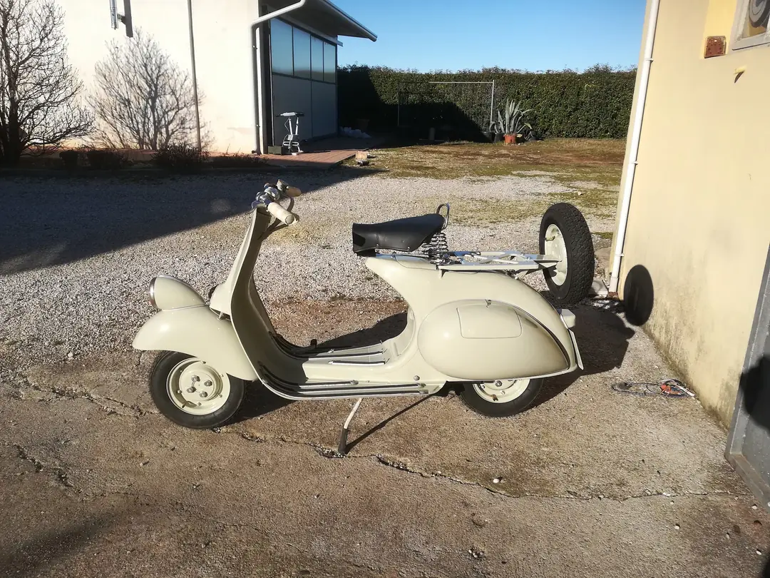Vespa d’epoca color crema con la ruota di scorta sul fianco